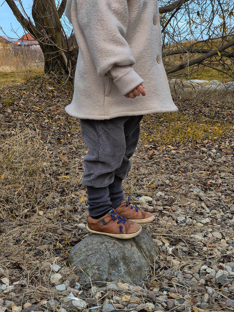 Kind trägt Knickerbocker Breitcord Stretch - Maus, passend für kühle Tage. Die graue Cordhose ist locker geschnitten und bequem, ideal für viel Bewegungsfreiheit beim Spielen im Freien.