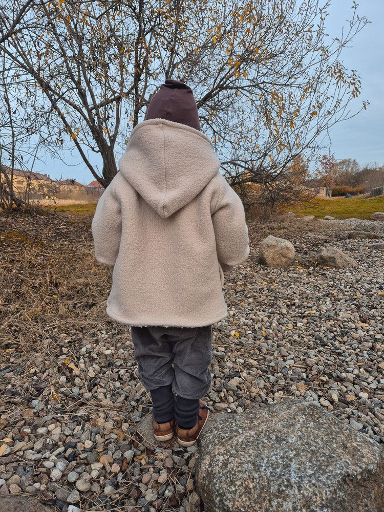 Kind, von hinten gesehen, trägt eine Knickerbocker Breitcord Stretch - Maus. Die Hose hat einen lockeren Schnitt, ideal zum Spielen und Entdecken, kombiniert mit einer beigen Jacke und brauner Mütze.