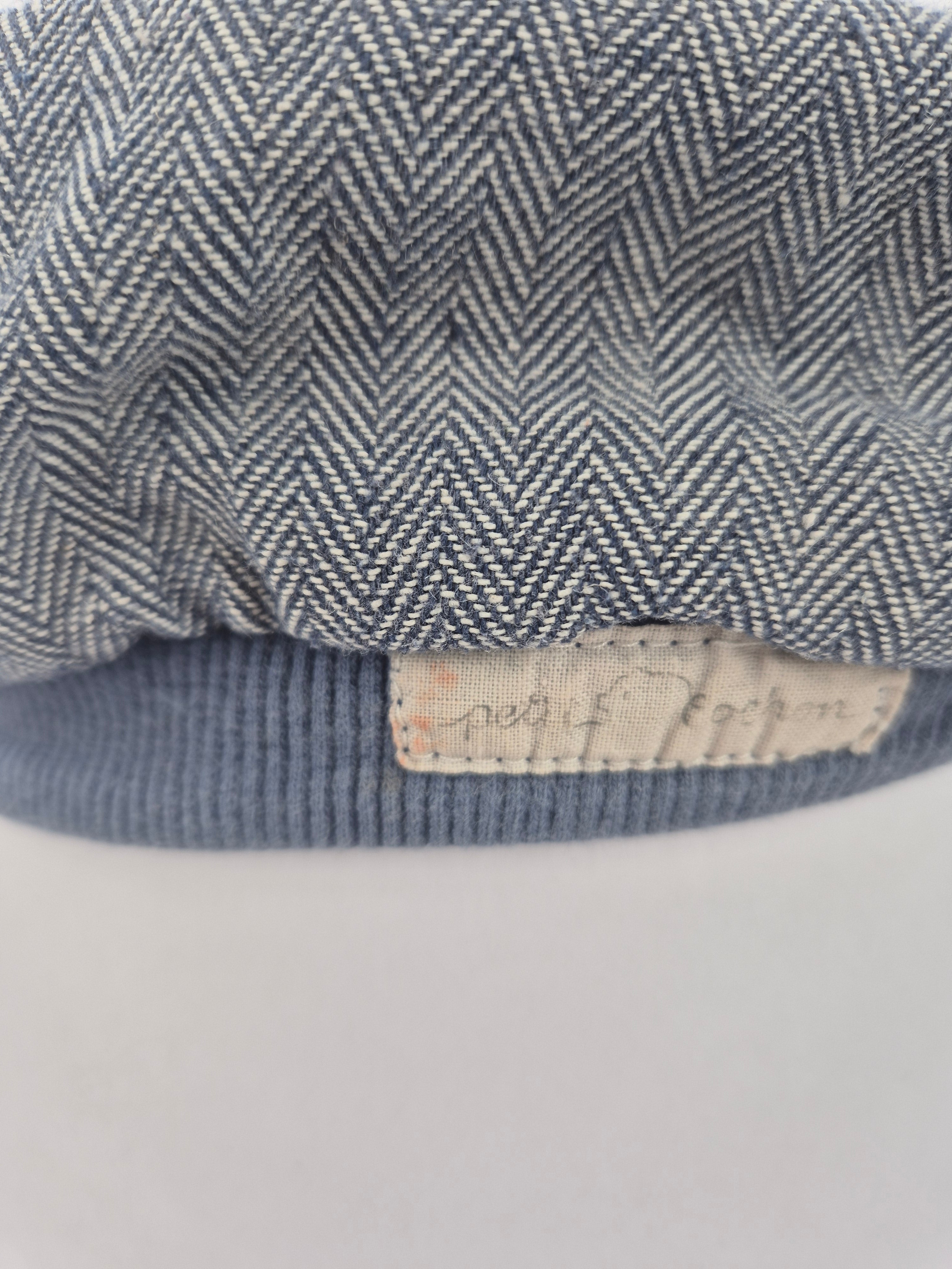 Nahaufnahme einer Michelmütze Fischgrat Blaubeere Gr. S-L mit Fischgrätmuster, geripptem Strickbund und einem kleinen Stoffetikett am Bündchen, Zustand: gut, ideal für Babys oder Kleinkinder.