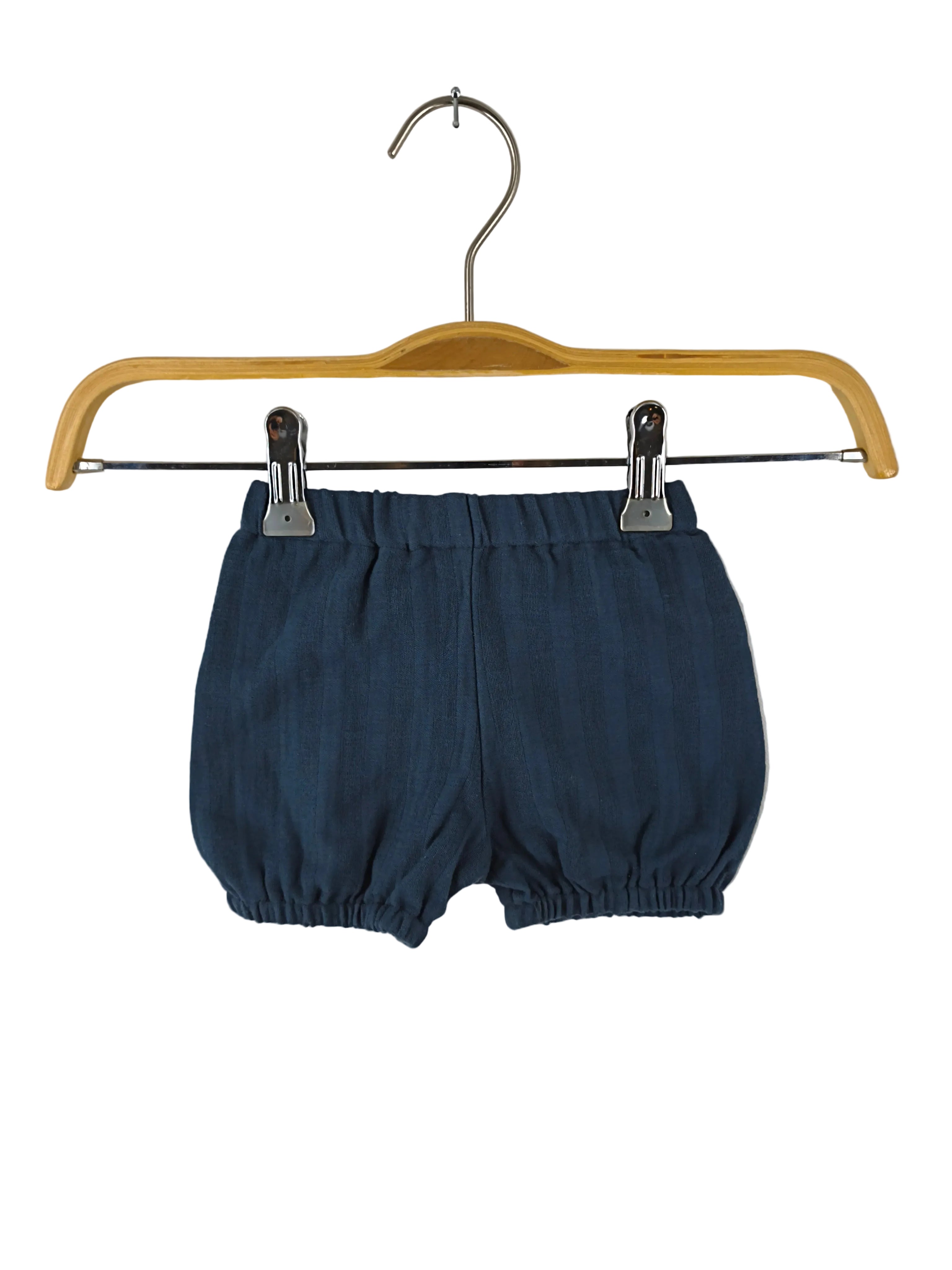 Kopie Kurze Pumphose Musselin Blaubeere Gr 3M, dunkle elastische Baby-Bloomers, hängen an einem einfachen Holzbügel mit Metallclips vor weißem Hintergrund. Zustand: sehr gut.