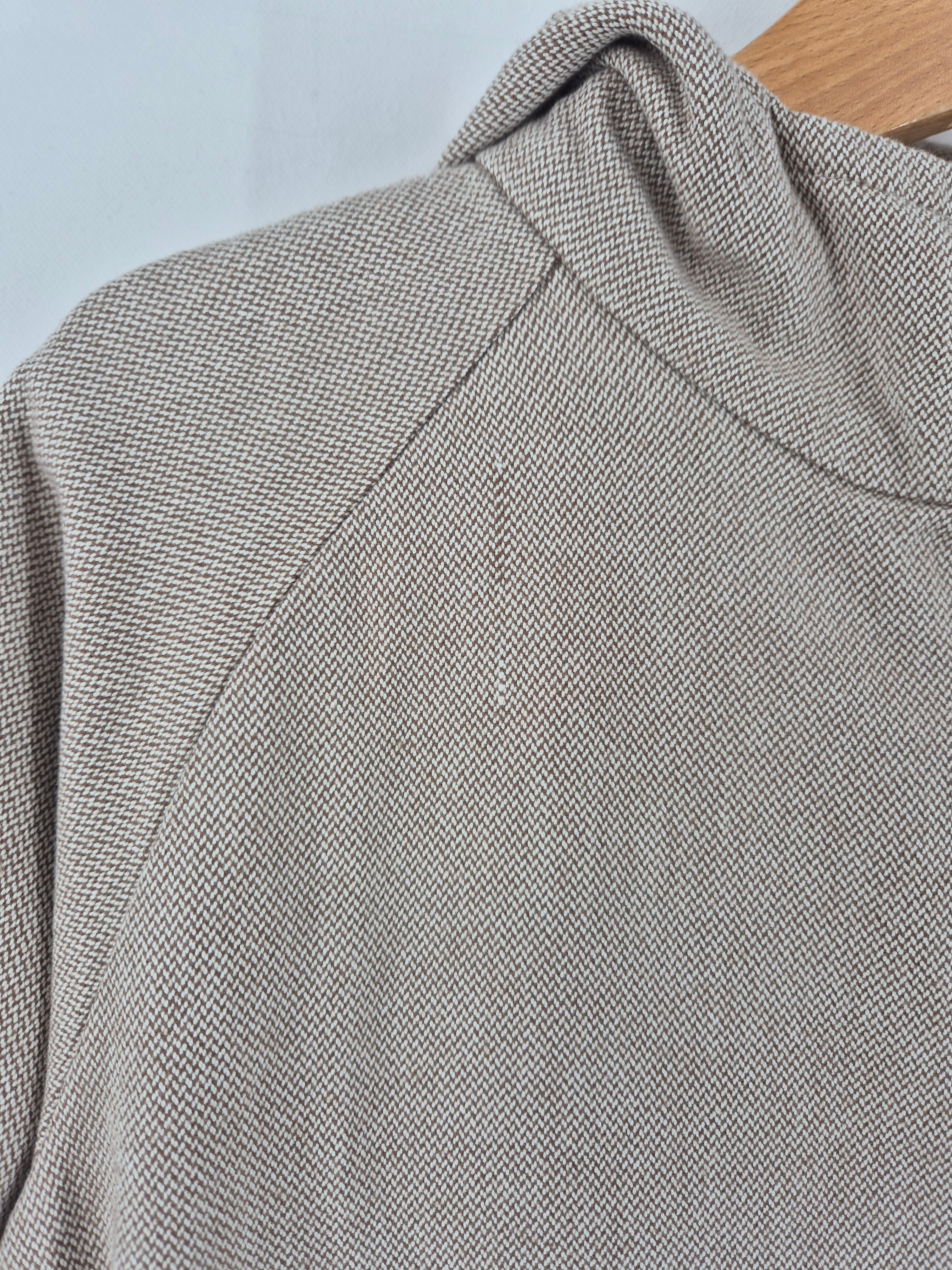 Nahaufnahme der Wichteljacke Kreuzköper Schlamm Gr. 3Y, leicht beige mit fein strukturierter Strickoptik, auf einem Holzkleiderbügel. Sichtbar sind die Schulternaht und der hohe Kragen. Zustand: sehr gut.