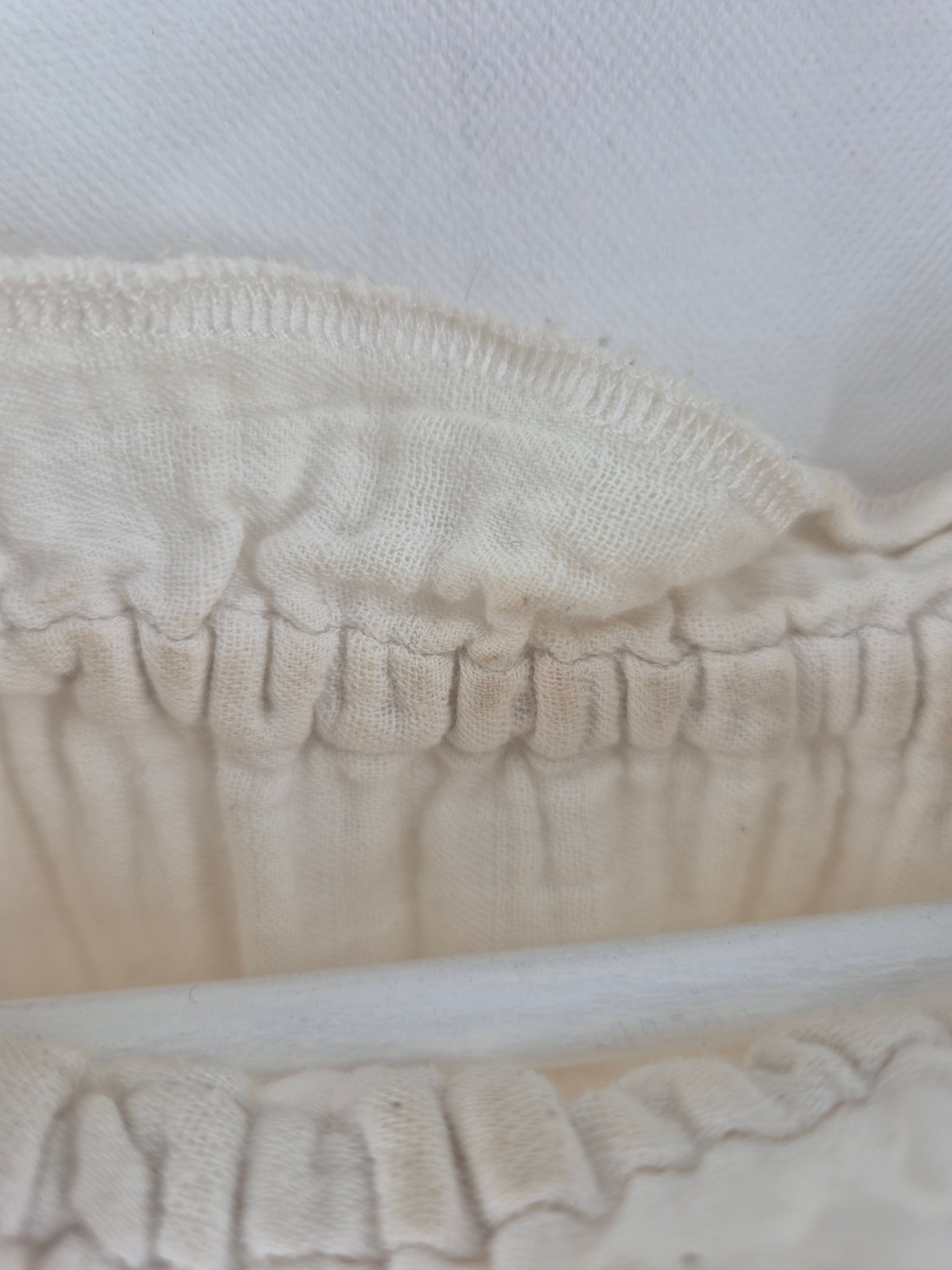 Nahaufnahme der Bluse Bio Musselin Natur mit gerafftem, off-white Baumwollstoff. Sichtbare Überwendlichnaht, elastische Raffnähte und ein weißer Stab hinter dem unteren Raffbereich. Zustand: gut mit kleinen Makeln.