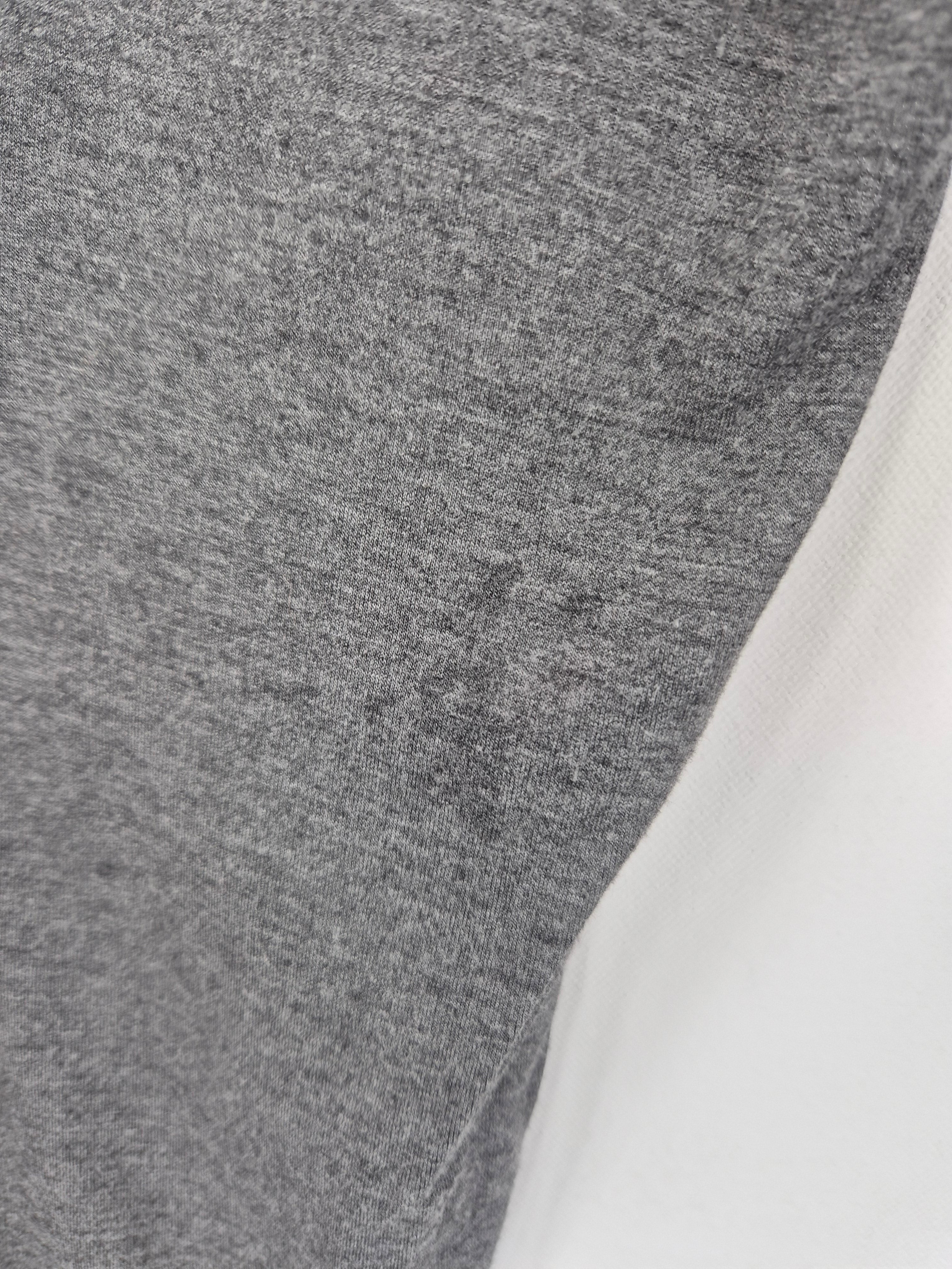 Nahaufnahme eines Wickelshirts Viskose Grau Gr. M mit heather-grauem Körper und weißen Raglanärmeln. Sichtbare dunkle Flecken auf dem grauen Stoff und am Ärmel. Zustand: sehr gut.