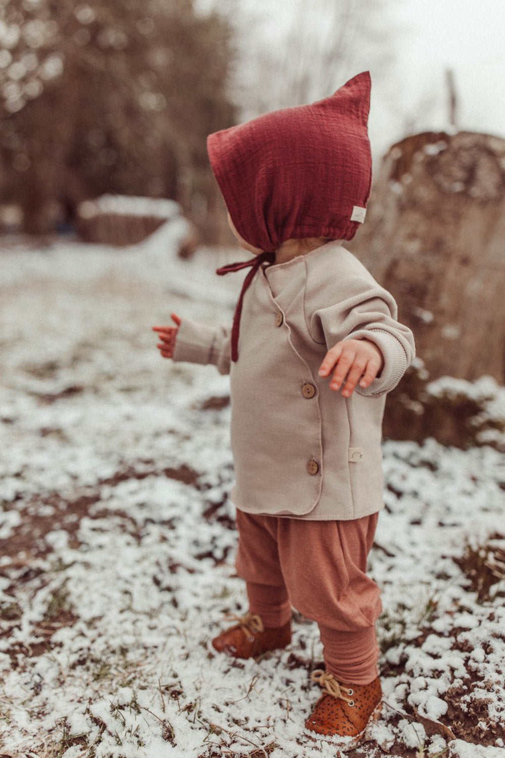 Babyknicker Kaschmir-Mix - Zimt: Baby in warmer Kaschmir-Mix-Hose mit Klappbündchen, steht im Schnee. Kombiniert mit passendem Loopbody für optimalen Komfort und Wärme.