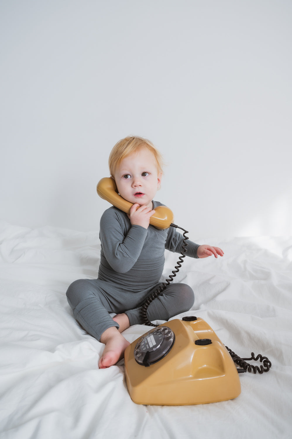 Baby mit einem Telefon am Ohr liegend, trägt eine Babyknicker Kaschmir-Mix - Taube, bekannt für ihre weiche, wärmende Passform mit praktischen Umklappbündchen, ideal für Neugeborene. Erstausstattung Baby und Geschenk für Babys.