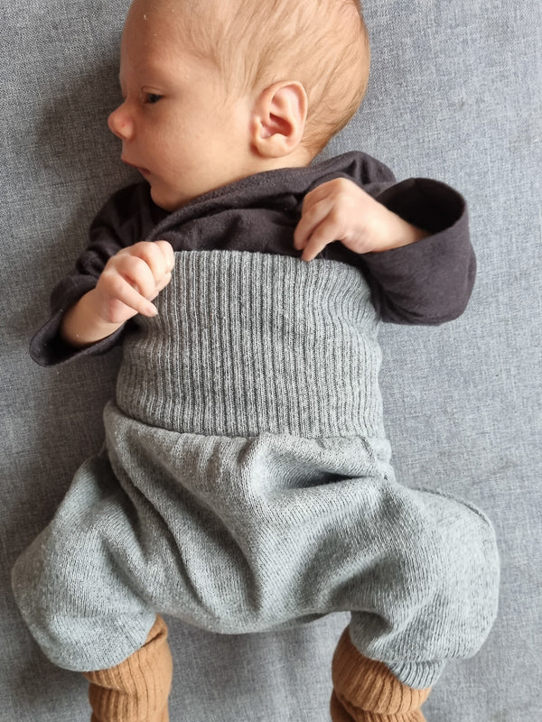 Babyknicker Strick - Maus: Ein Baby liegt auf einer Decke, trägt eine kuschelig weiche Strickhose aus 100% recycelter Baumwolle mit elastischen Bündchen.