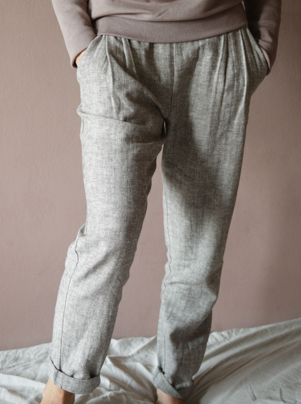 Eine Person trägt eine Bundfaltenhose Fischgrat, die durch ihre klare Struktur und den lässigen, doch eleganten Schnitt auffällt. Die Hose zeigt eine dezente Textur, die dem Design Tiefe verleiht.