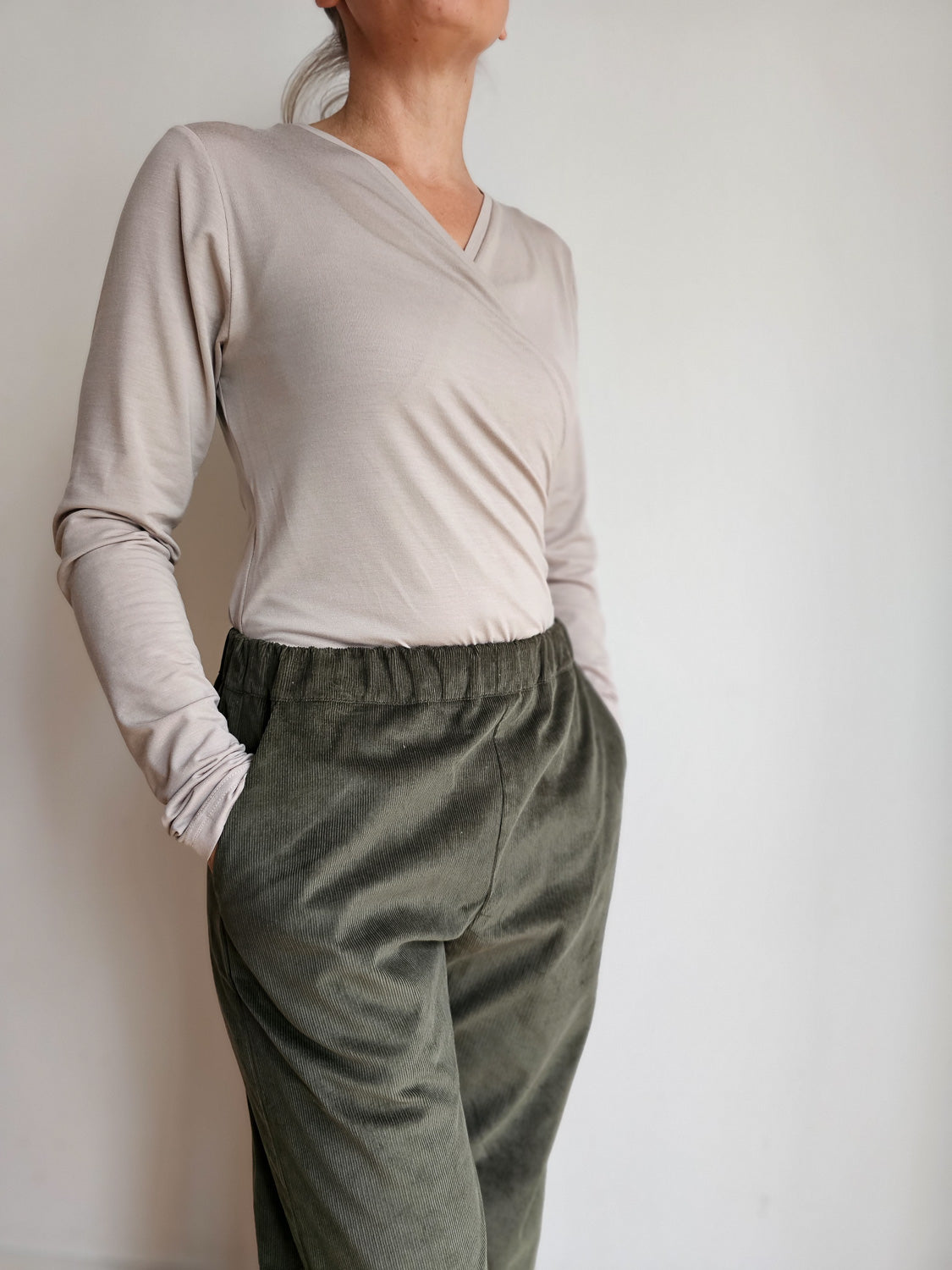 Frau trägt Wickelshirt Langarm Kaschmir-Mix - Sand, Hände in den Taschen. Weiches, atmungsaktives Material, ideal zum Stillen.