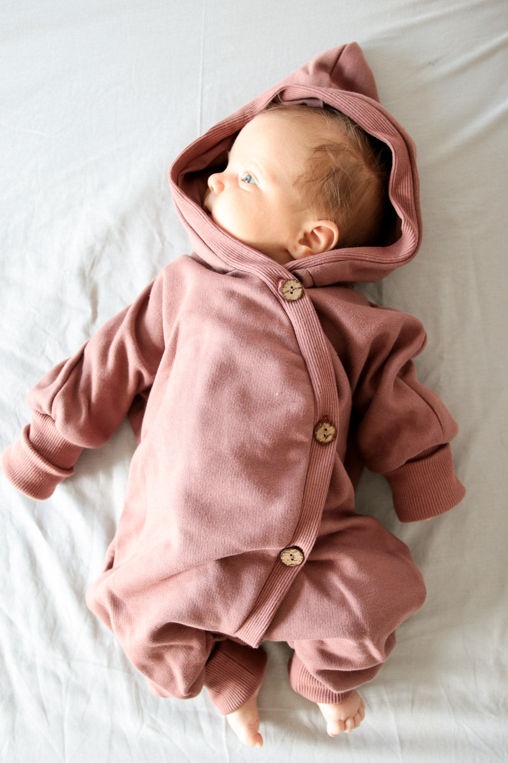 Kuschelanzug Bio-Sweat - Zimt: Ein Baby trägt einen weichen, kuscheligen Anzug mit Wichtelkapuze, ideal für drinnen und draußen. Der Overall wächst mit dank Krempelbündchen an Armen und Beinen.  Erstausstattung Baby und Baby Geschenk zur Geburt.