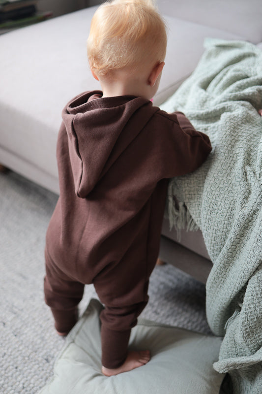 Kleinkind auf Couch in Kuschelanzug Bio-Sweat - Schoko mit Wichtelkapuze, bequem und weich, ideal für drinnen und draußen an kühlen Tagen.