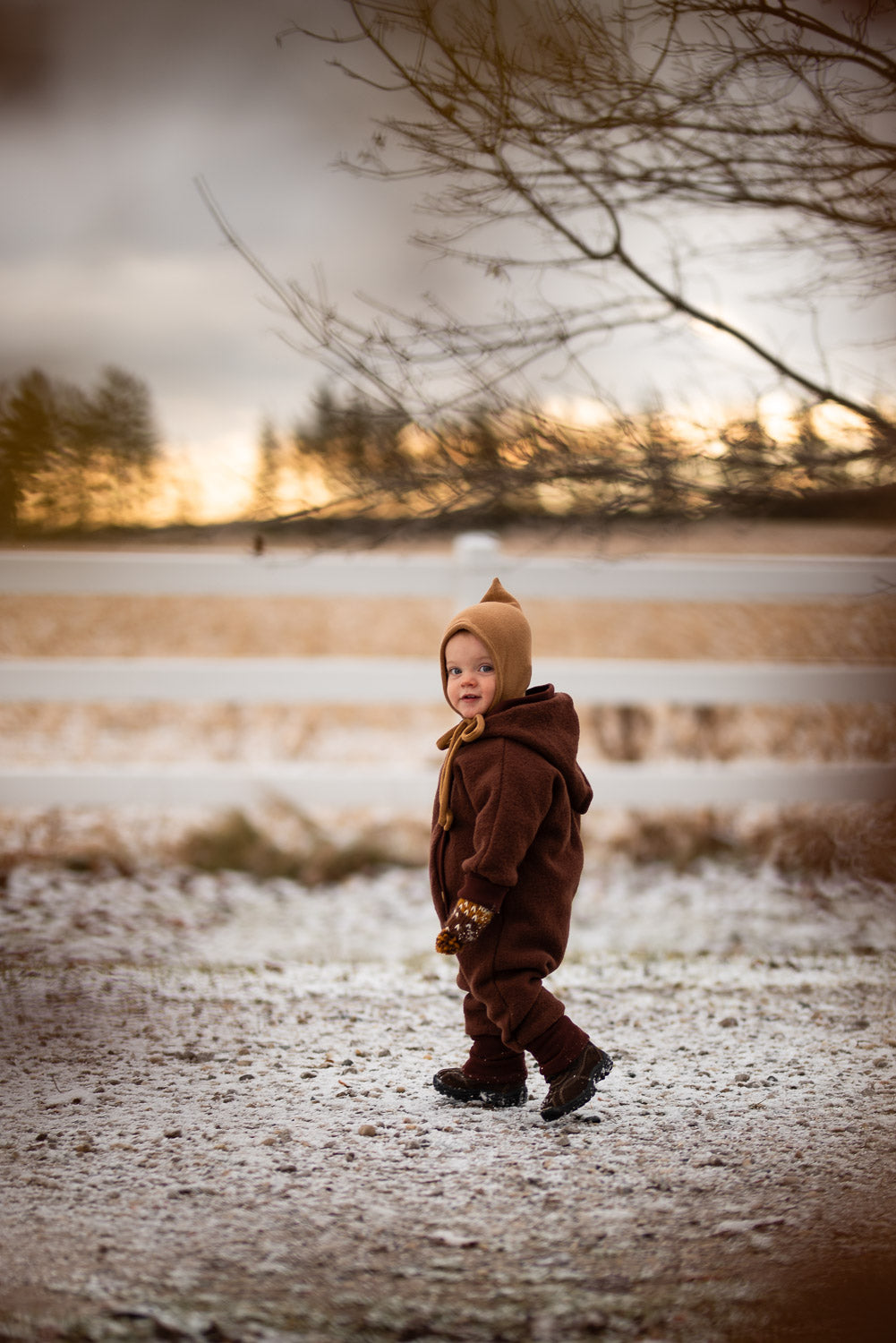 Niño con mono de peluche de lana hervida de Teddy, en color castaño, caminando por la nieve. El mono ofrece calidez y libertad de movimiento, ideal para los fríos días de invierno.