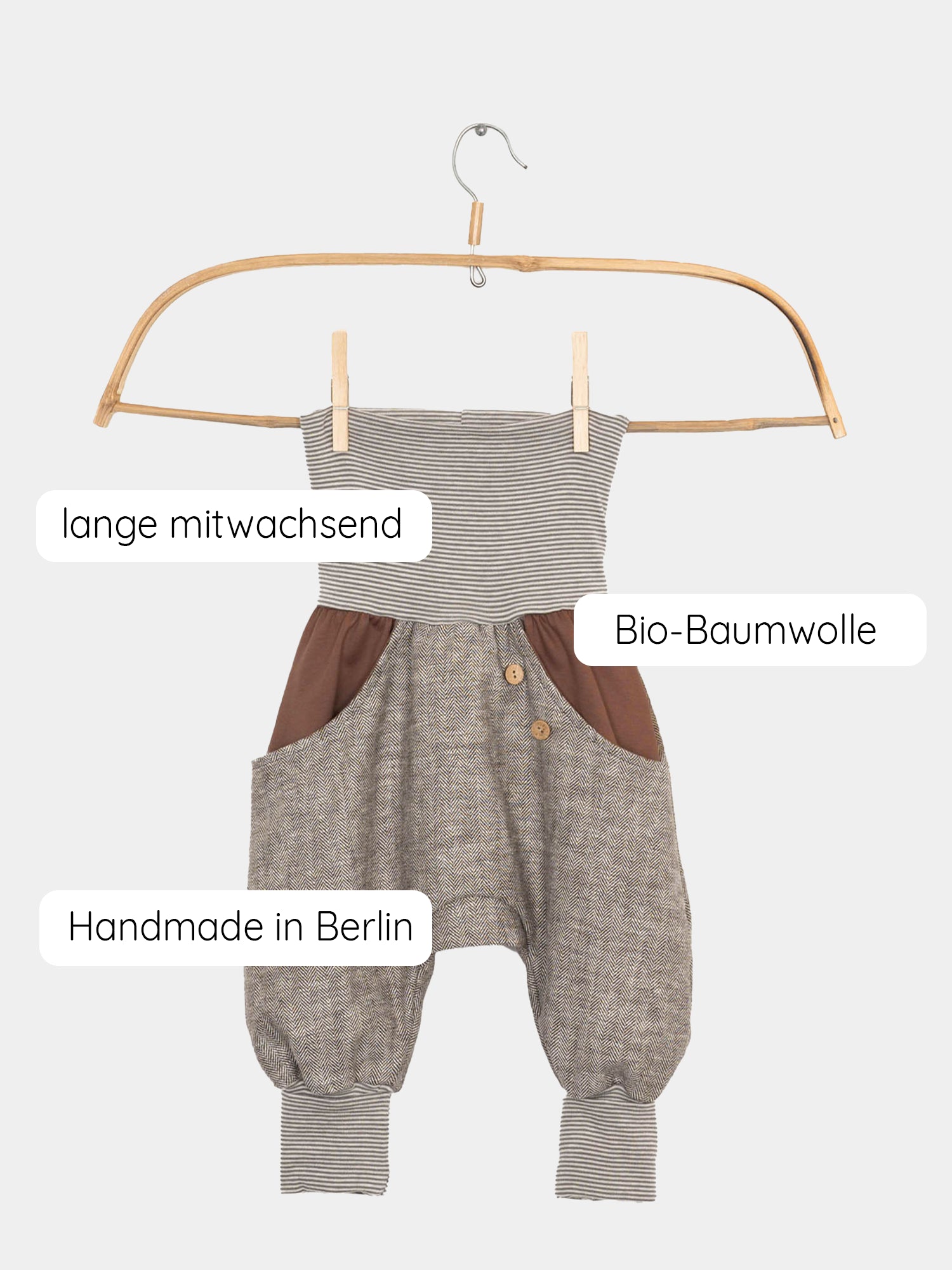 Knickerbocker Fischgrat - Schoko: Ein gestreiftes Kleidungsstück hängt auf einem Kleiderbügel, ergänzt durch braune Hosen mit Knöpfen, zeigt die markanten Texturen und Details der robusten Naturfaser.
