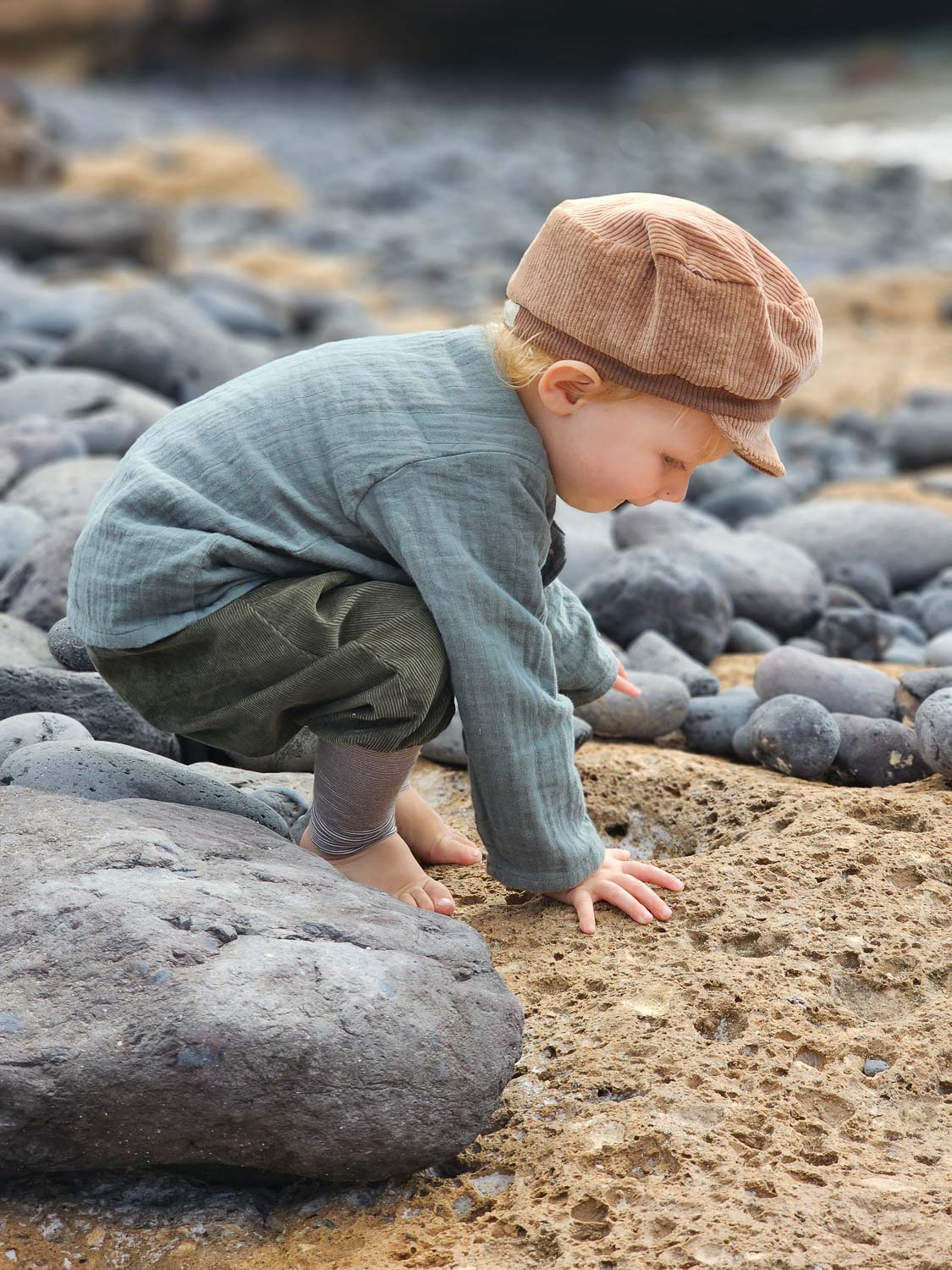 Ein Kind spielt auf Felsen und trägt das Hemdchen Bio-Musselin - Taube aus luftiger Bio-Baumwolle, ideal für Alltag und besondere Anlässe. nachhaltige Kinderkleidung
