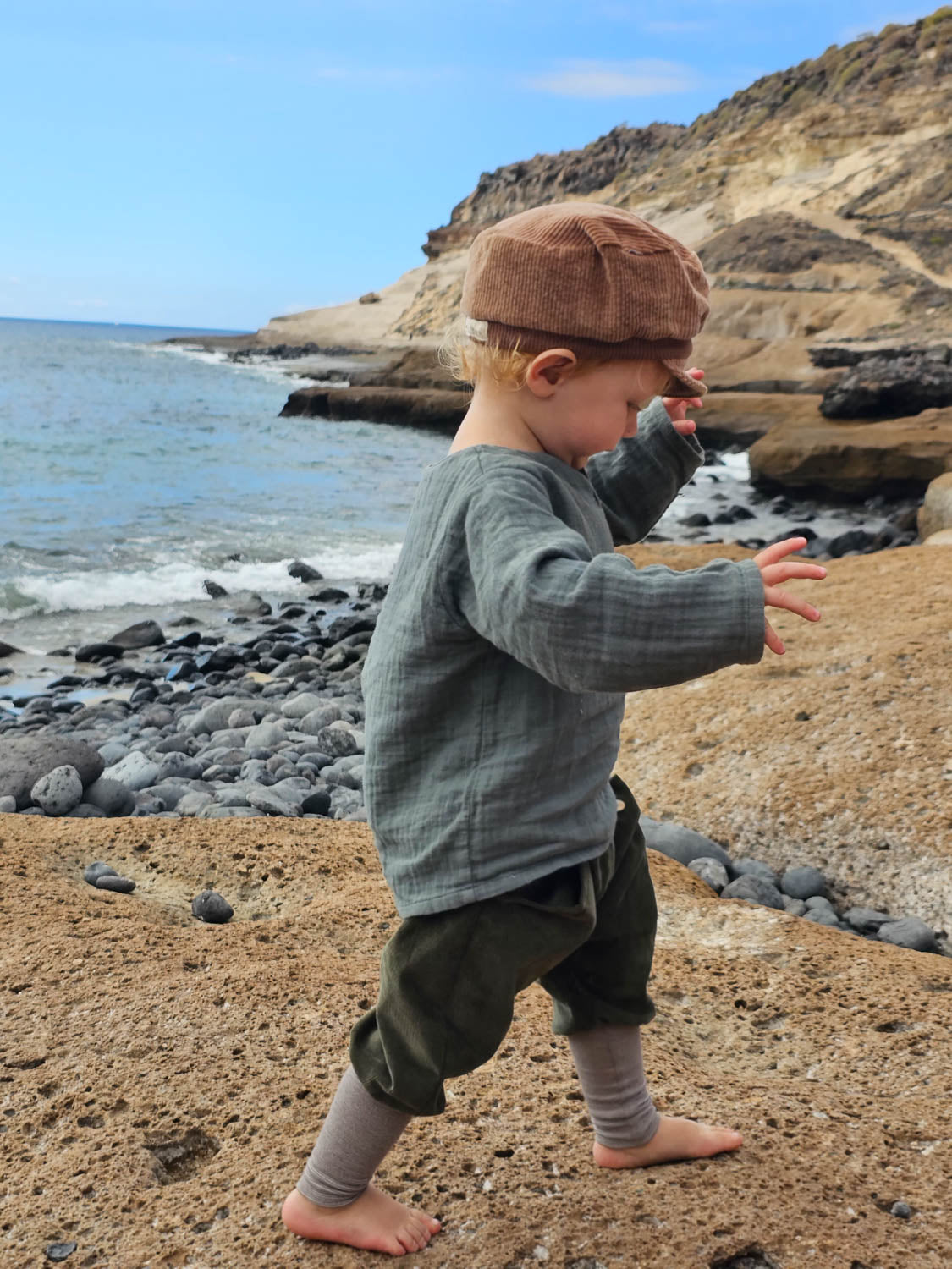 Kind trägt Hemdchen Bio-Musselin - Taube, spaziert auf Felsen am Wasser. Leichtes, vielseitiges Shirt aus 100% Bio-Baumwolle, handgefertigt in Berlin.
