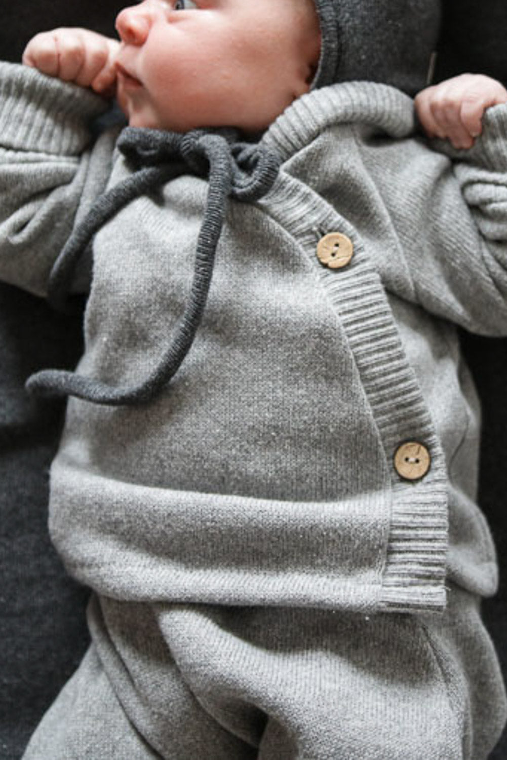 Baby in grauem Babyschlüttli Strick - Maus aus recycelter Baumwolle, flauschig angeraut, mit Krempelbündchen, geeignet für Jungen und Mädchen, hergestellt in Berlin. Erstausstattung Babys. Perfekte Baby Geschenke.