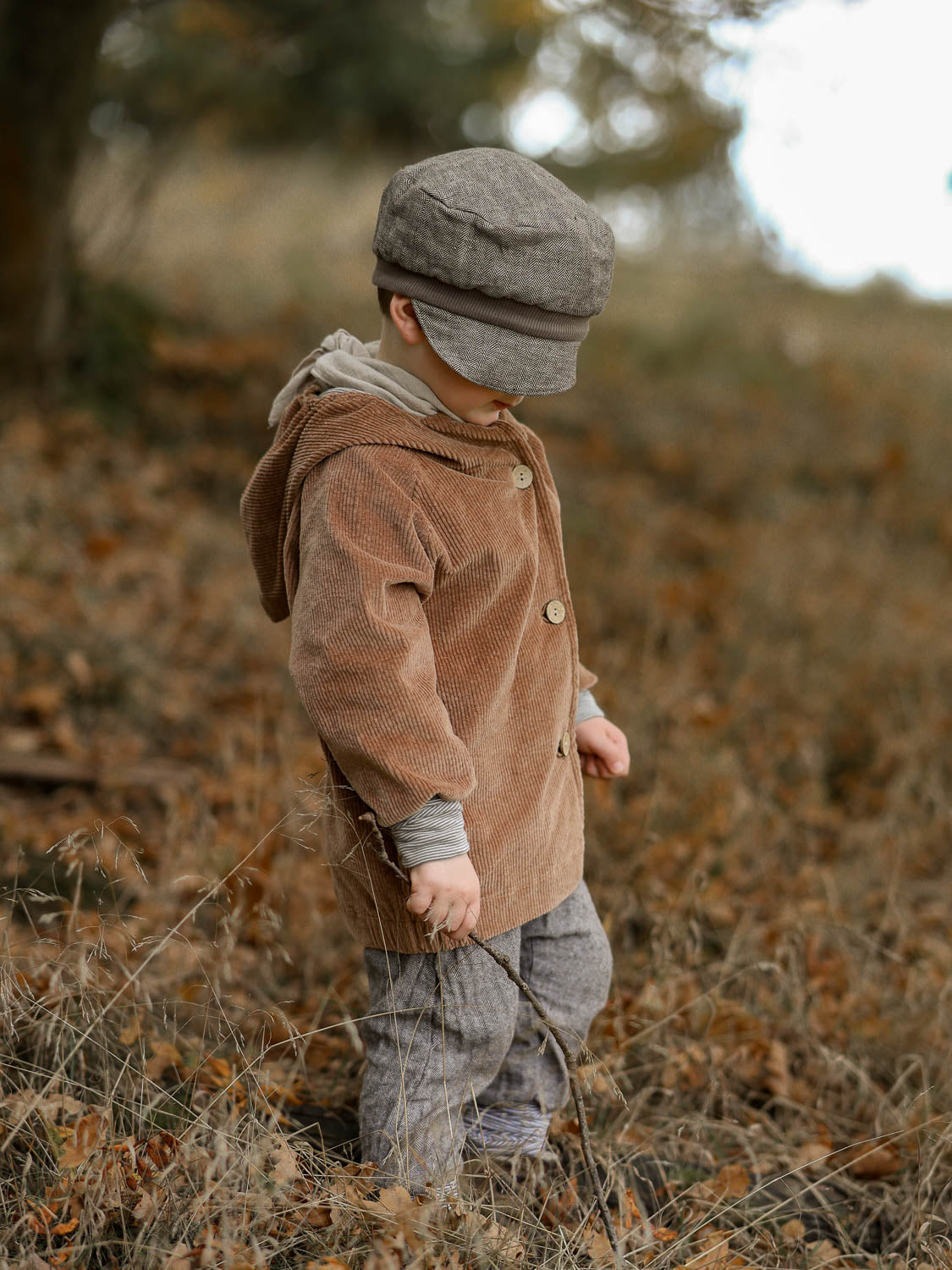 Kind in einem Feld mit Wichteljacke Breitcord - Weizen, featuring krempelbare Ringel-Armbündchen und Wichtelkapuze, ideal für komfortables Wachstum. Handgefertigt in Deutschland.